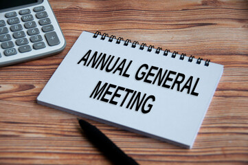 Annual general meeting text on notepad with calculator, pen and wooden table background.