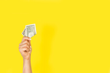 Mano de mujer sosteiendo un billete dolar sobre un fondo amarillo liso y aislado. Vista de frente y de cerca. Copy space