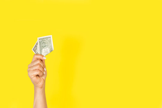Mano de mujer sosteniendo un billete dolar sobre un fondo amarillo liso y aislado. Vista de frente y de cerca. Copy space