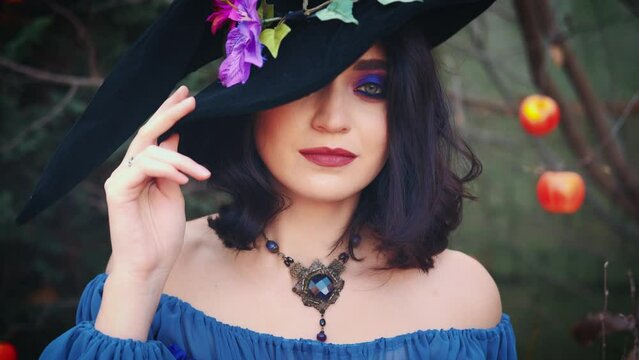 Close-up portrait sexy face, blue eyes creative design festive art makeup, girl looking at camera. Fantasy Woman Old Style Medieval Witch Halloween Costume Black Pointed Cone Hat Carnival Purple Dress