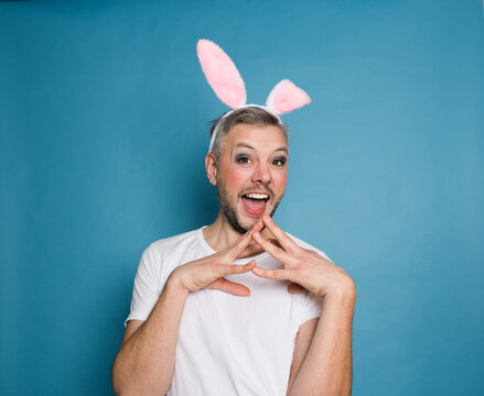 An LGBT gay man smiles on a blue background with rabbit ears on his head