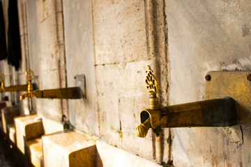 Selective ablution place for Muslims in Istanbul. Fountain made of yellow brass, on blurred limestone wall. 