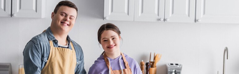 Smiling teenagers with down syndrome looking at camera in kitchen, banner.