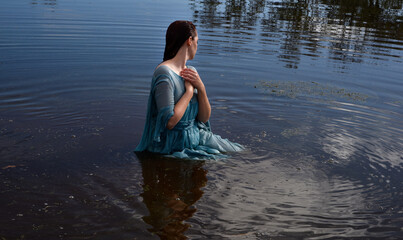 Fototapeta premium Portrait of beautiful girl wearing flowing fantasy gown in a magical lake background.