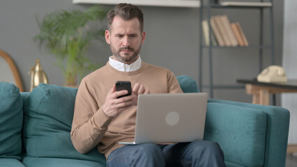 Man with Laptop using Smartphone on Sofa 