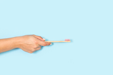 Mano de mujer sosteniendo un cepillo de dientes de bambú sobre un fondo celeste liso y aislado. Vista de frente. Copy space