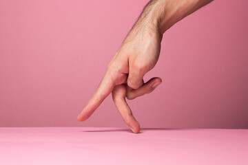 The male hand imitates stepping with fingers. Fingers step on a pink background. hand gesture