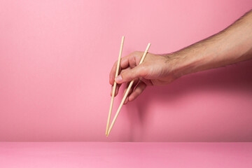 Male hands hold oriental Chopsticks on a pink background. Wooden Chinese chopsticks for Asian dishes.