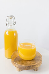 Fresh squeezed orange juice in bottle and glass on wooden tray on table, white background. Healthy beverage for breakfast. Side view, copy space