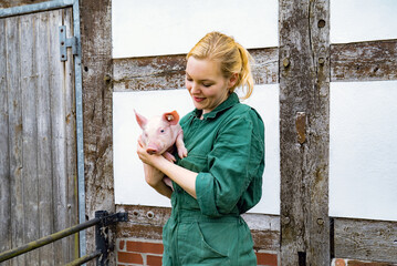 Begeisterung für Schweine - junge Frau mit einem niedlichen Ferkel im Arm, landwirtschaftliches...