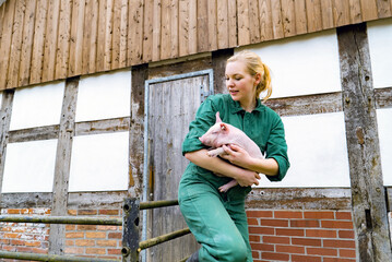 Begeisterung für Schweine - junge Frau mit einem niedlichen Ferkel im Arm, landwirtschaftliches...