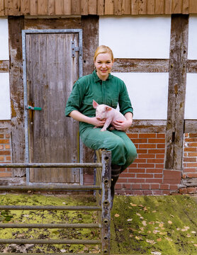 Begeisterung für Schweine - junge Frau mit einem niedlichen Ferkel im Arm, landwirtschaftliches Symbolfoto.