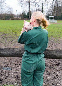  Spass an der Schweinehaltung - junge Landwirtin trägt lässig ein Ferkel auf der Schulter, landwirtschaftliches Symbolfoto.