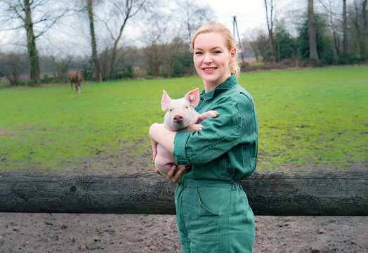 Begeisterung für Schweine - junge Frau mit einem niedlichen Ferkel im Arm, landwirtschaftliches Symbolfoto.