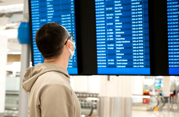 Closeup of Young unrecognizable man in the mask in airport near flight timetable. Travelling in the pandemic concept