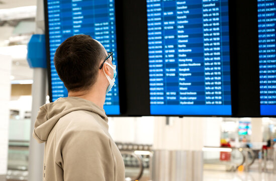 Closeup of Young unrecognizable man in the mask in airport near flight timetable. Travelling in the pandemic concept