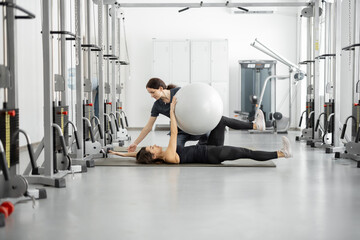 Fototapeta na wymiar Woman doing exercises with fitness ball with rehabilitation specialist at the gym. Concept of physical therapy for health and recovery. Idea of recovery after pregnancy