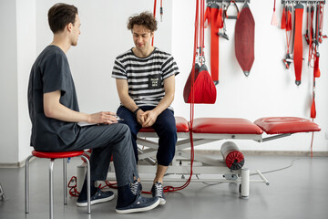 Man having consultation with rehabilitation specialist or physiotherapist before active treatment on suspension straps