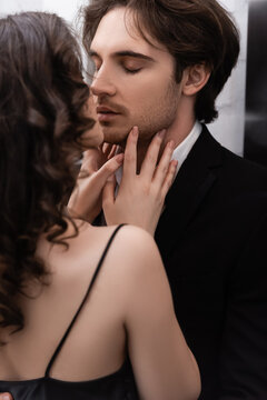 curly young woman kissing man in blazer.