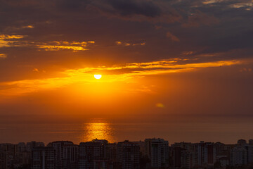 The sun coming out from behind the clouds. Sunset over the city by the sea.