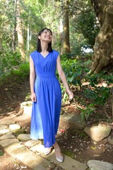初夏の新緑を背景に微笑む青いドレスを着た微笑む若い女性	