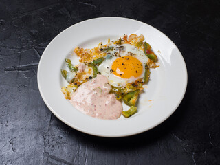 Fried eggs on a round white plate on a black background. Studio photography
