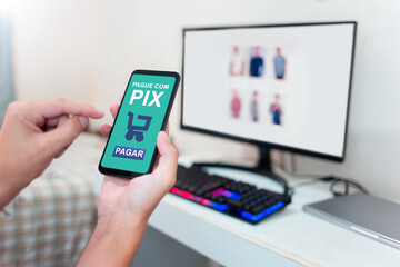 Hands holding smartphone to pay for online purchases through Pix. Shopping online on computer and using mobile app for instant payment