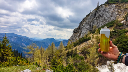 Person holding a can of beer with panoramic view on the mountain peaks of the Hochschwab Region in...