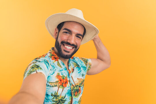 charming young Latino American man in Hawaiian clothes takes a selfie orange background medium closeup studio shot . High quality photo