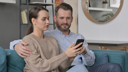 Fototapeta premium Portrait of Couple using Smartphone While Sitting on Sofa 