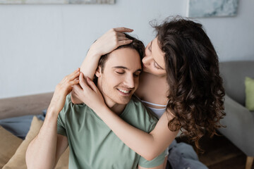 Fototapeta premium curly woman kissing forehead of happy boyfriend.