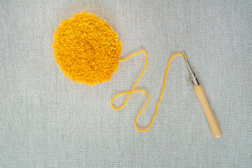 Round yellow tufted flower on textured linen fabric and a punch needle with yellow thread, which...