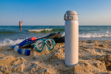 White thermo water bottle for summer leisere. Flask thermos of drinks on sand on background of...