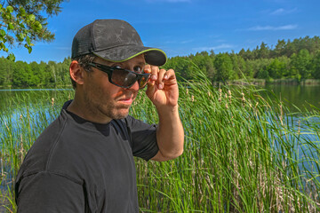 Skeptical look. Man in cap watches from under sunglasses with contempt, doubtful and scepticism outdoors
