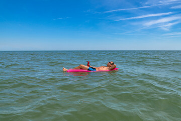 Tanned man relax on pink inflatable mattress at sea. Successful Guy in sunglasses enjoying vacation and cool drinks