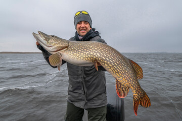 Success pike fishing. Happy fisherman with big fish trophy at boat - obrazy, fototapety, plakaty