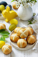 Happy Easter festive food concept. Homemade Easter traditional hot cross buns with raisin and natural colorful easter eggs on a rustic table.
