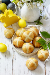 Happy Easter festive food concept. Homemade Easter traditional hot cross buns with raisin and natural colorful easter eggs on a rustic table. Copy space.