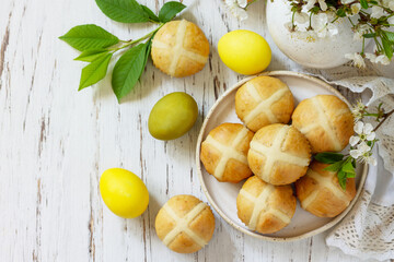 Happy Easter festive food concept. Homemade Easter traditional hot cross buns with raisin and natural colorful easter eggs on a rustic table. Top view flat lay. Copy space.