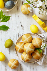 Happy Easter festive food concept. Homemade Easter traditional hot cross buns with raisin and natural colorful easter eggs on a rustic table. Top view flat lay. Copy space.