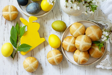 Happy Easter festive food concept. Homemade Easter traditional hot cross buns with raisin and natural colorful easter eggs on a rustic table. Top view flat lay. Copy space.