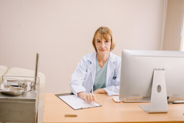 A female dentist sits in her office and looks at the camera in a friendly manner.
