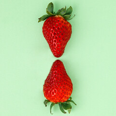 Two strawberries facing each other on high pastel green background. Simple square composition.