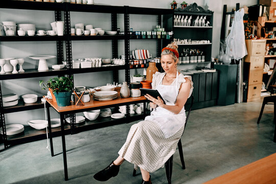 Checking my schedule for the day. Cropped shot of an attractive mature woman sitting alone and using a tablet in her pottery workshop.
