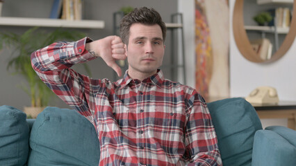 Portrait of Man Showing Thumbs Down while Sitting on Sofa 