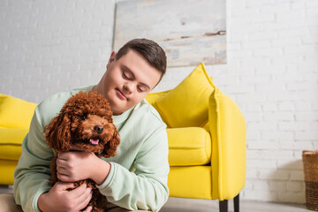 Teen boy with down syndrome hugging brown poodle at home.