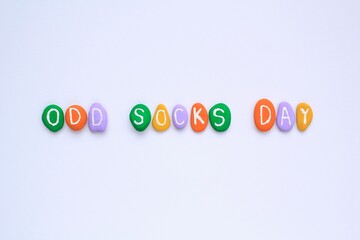 Fototapeta premium Odd socks day lettering on colorful stones pebbles on white background. Social school bullying concept. Lost lonely socks. Top view flatlay idea for poster, banner, advertising