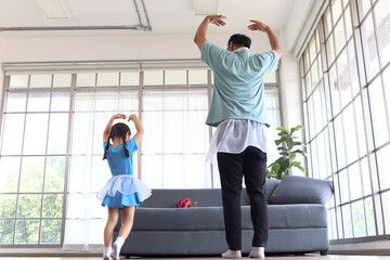 Adorable cute little girl with young cheerful handsome dad wear beautiful skirt, dance together, dad trying to train daughter to dance ballet, Happy family spending time together. Happy Father's Day