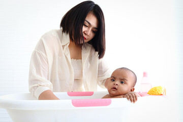 A six month African American infant baby taking bubble bath in bathroom, mother bathing kid in tub, mom washing and cleaning her child in bath.