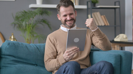 Man Celebrating Success on Tablet on Sofa 